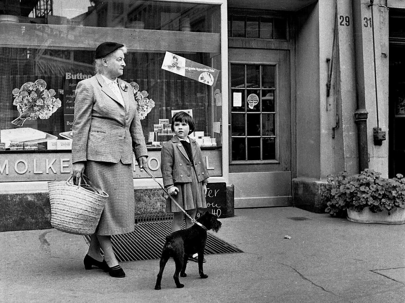 Frau mit Kind und Hund vor einem Geschäft mit Aufschrift: MOLKEREI HOFWYL. Schwarz-weiss Fotografie.