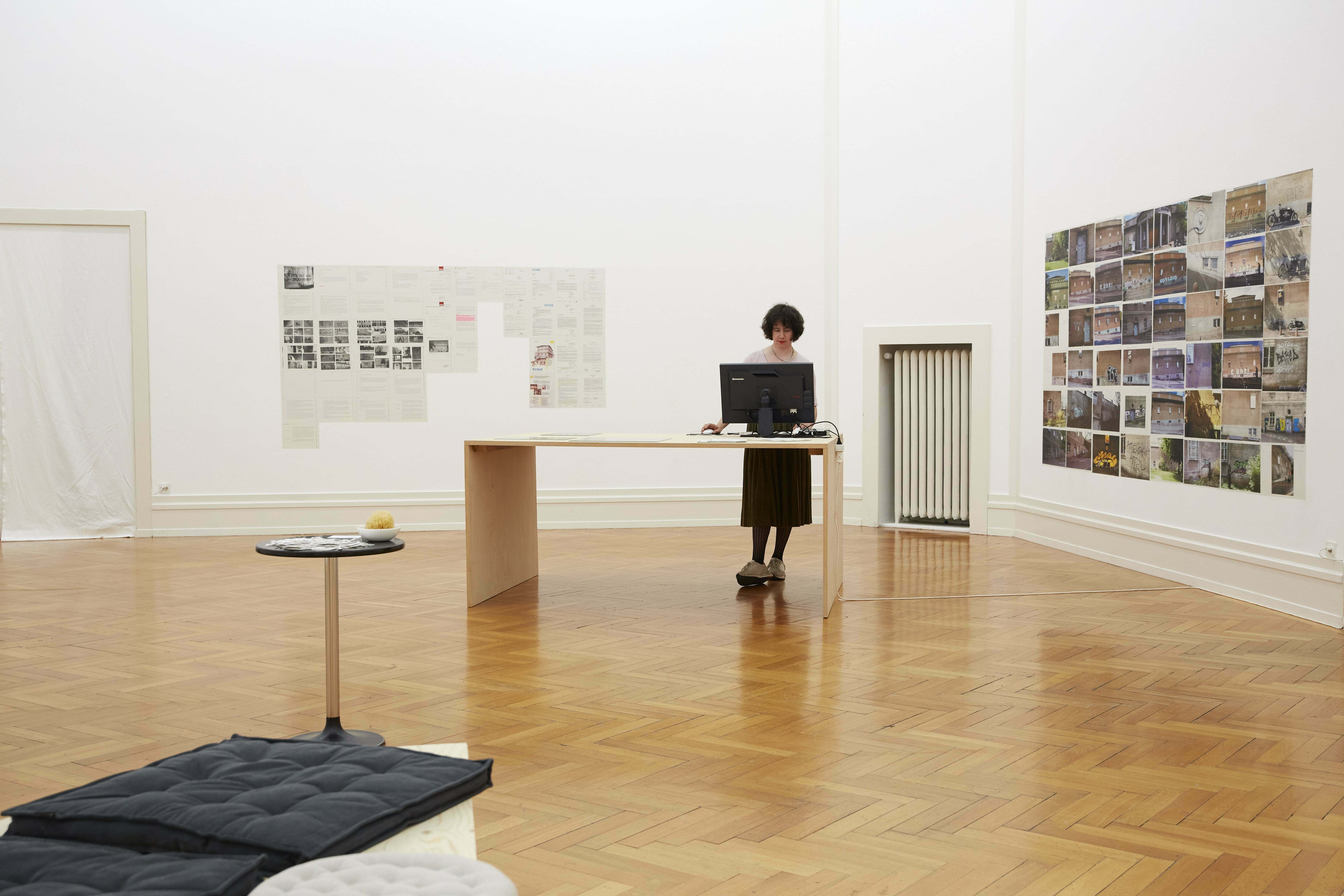 Blick auf die Kunsthalle. An der Wand hängen Bilder, im Zentrum steht eine Frau an einem Tisch mit einem Laptop.