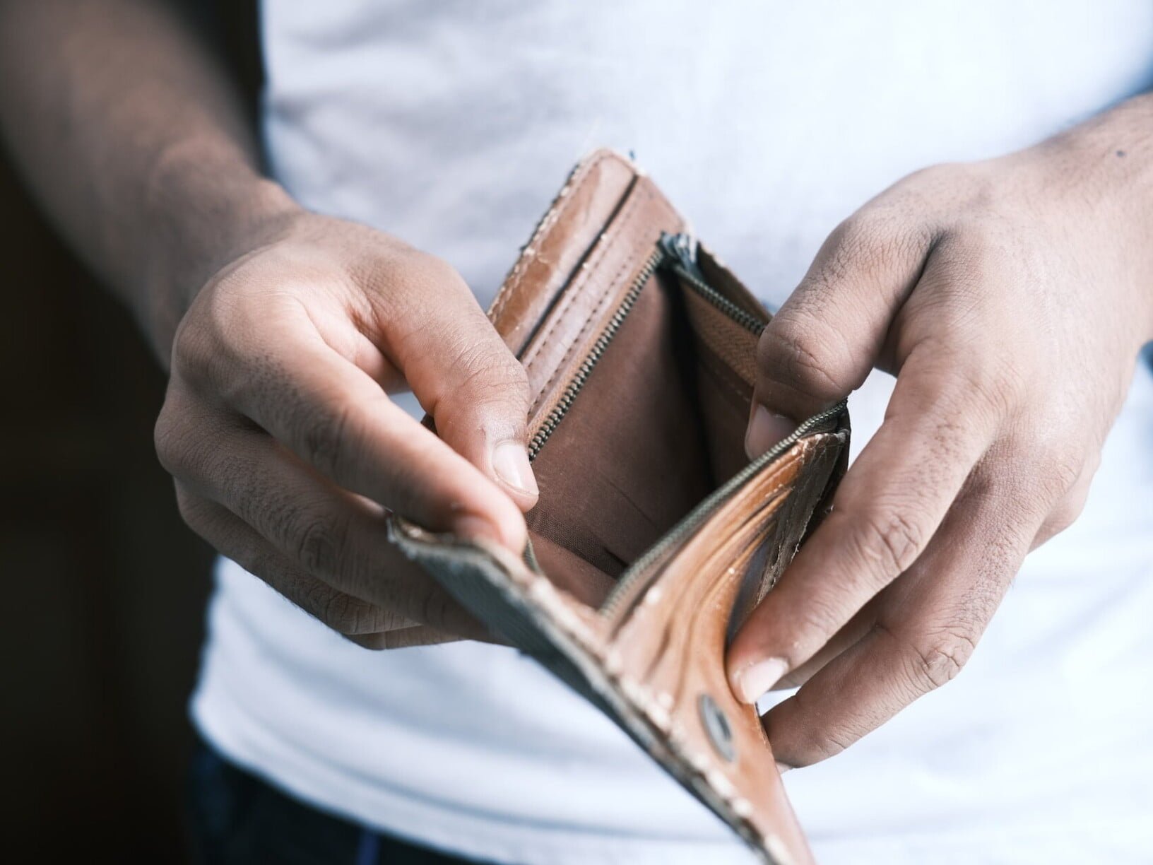 Eine Person im weissen T-Shirt zeigt eine braune, leere Brieftasche.