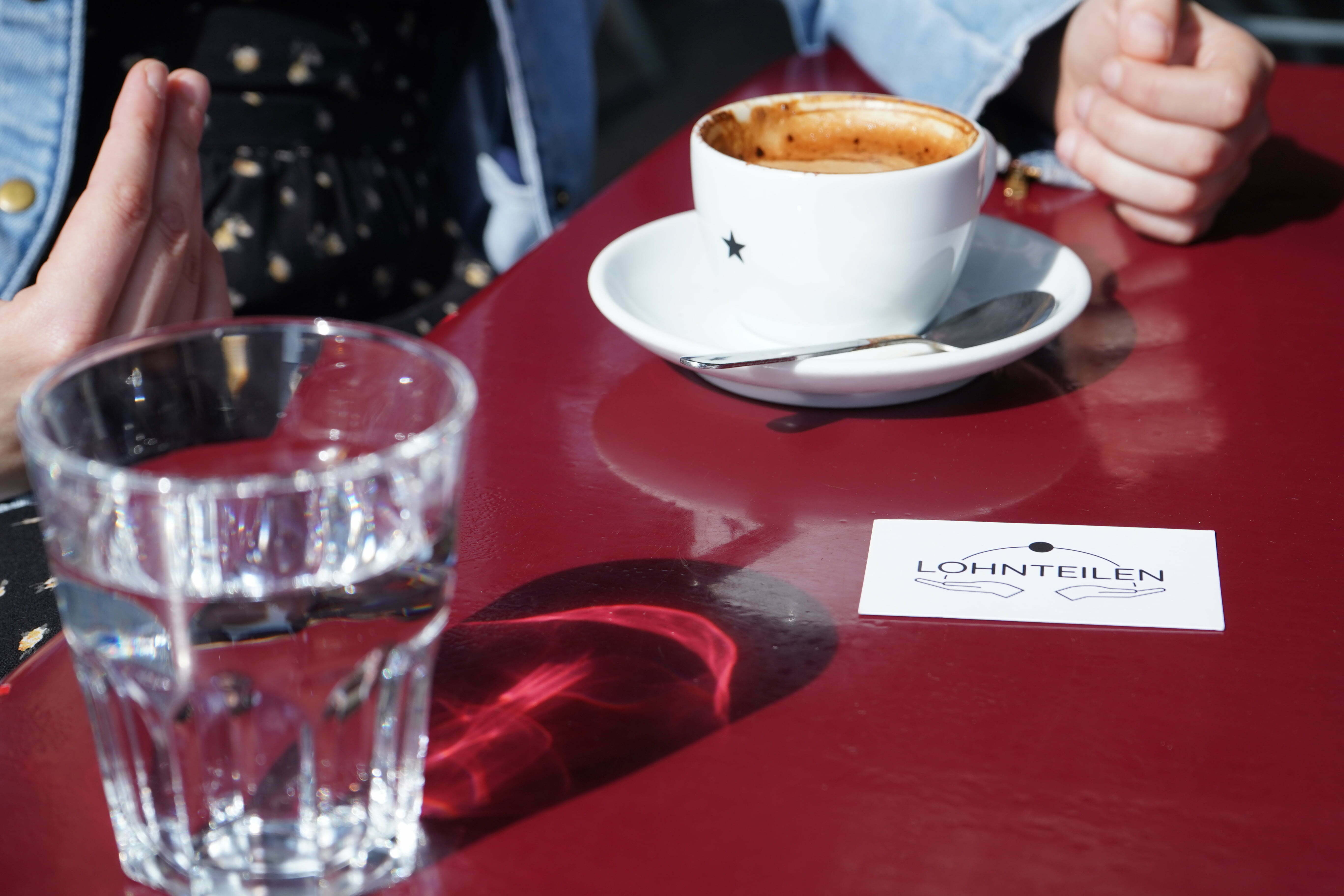Ein roter Tisch mit einem Kaffee, Wasser und einer Karte auf der «Lohnteilen» steht.