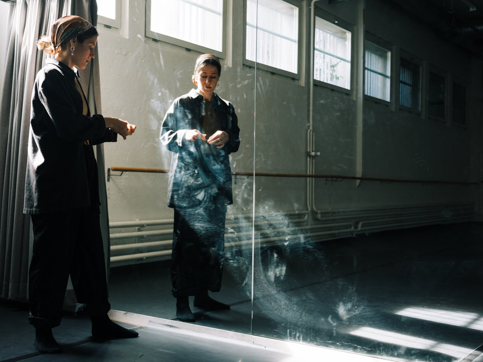 Eine Frau schaut nach unten in eine Spiegelwand. Sie trägt ein Kopftuch und Sportkleider.